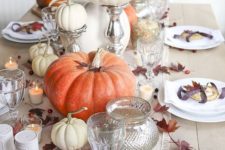 a cute fall or Thanksgiving table setting with pumpkins, fall leaves, cranberries and mini pies for each place setting