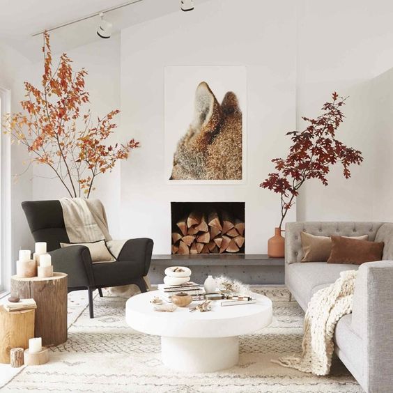 a fall Scandinavian living room with branches with leaves, faux fur, candles on tree stumps and a fox artwork