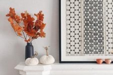 a fall mantel with a graphic artwork, fabric pumpkins and a black vase with fall leaves for natural decor
