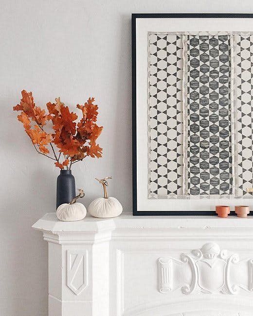 a fall mantel with a graphic artwork, fabric pumpkins and a black vase with fall leaves for natural decor