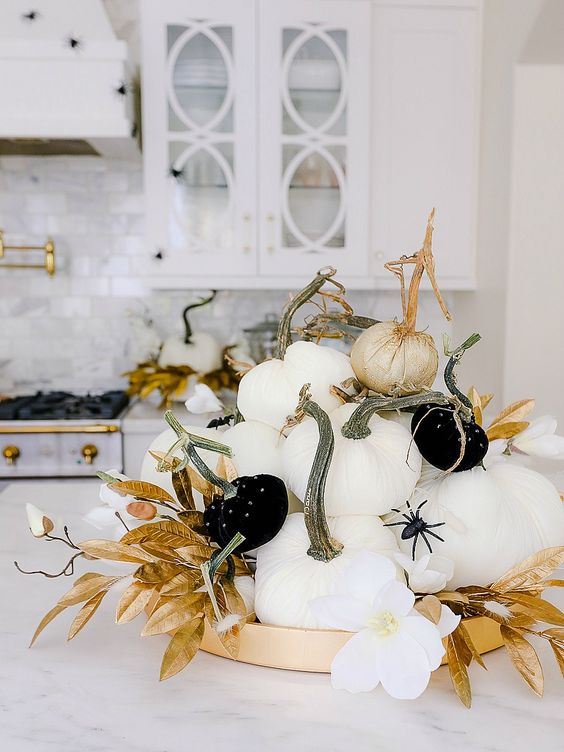 a glam Halloween centerpiece of white and black pumpkins with spiders, gold leaves and white blooms