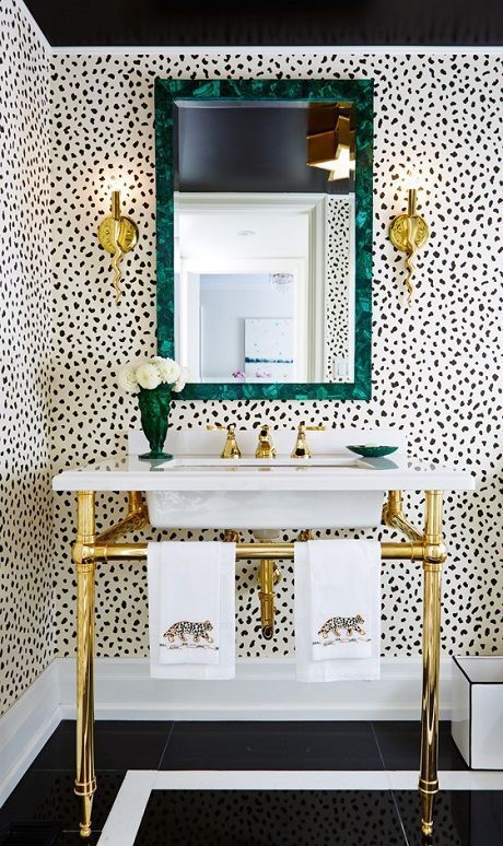 a glam bathroom with Dolmatin walls, a gold sink stand, gold sconces and a mirror in a beautiful green frame plus a green vase