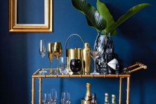a glam nook with a navy wall, a gold bamboo bar cart, gold empty frame decor on the wall is amazing