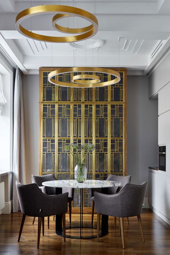 a jaw-dropping dining space with a gold and glass buffet, a marble table, grey chairs and gold circle pendant lamps