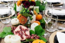 a lush table runner of foliage, berries, fruits, blooms, pillar candles and mini pumpkins for a Thanksgiving table