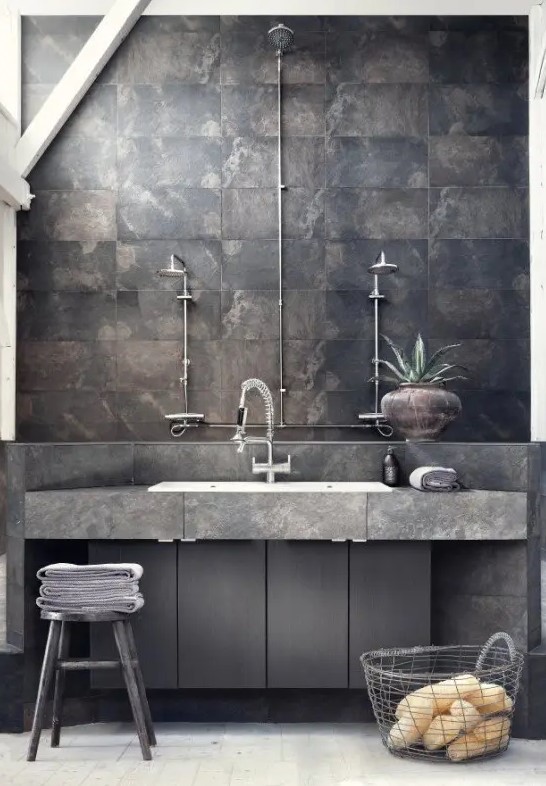 a minimalist industrial bathroom done with rusty tiles, concrete and sleke wooden surfaces, exposed pipes and wooden stools