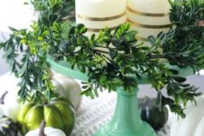 a modern and simple Thanksgiving centerpiece of a green stand, striped pillar candles, greenery, white and green pumpkins