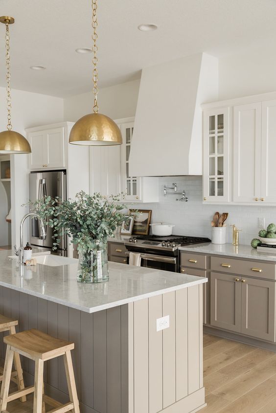 a modern farmhouse kitchen with white and taupe cabinets, white tiles and countertops, gold metal pendant lamps and gold fixtures
