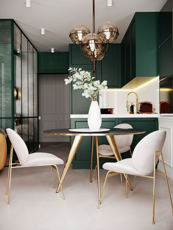 a modern refined space with dark green cabinets, a gold round table, creamy chairs with gold legs and gold fixtures that tie up two zones