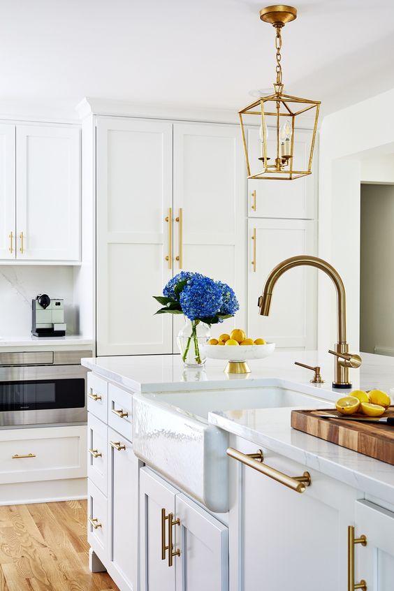 a modern white kitchen with a farmhouse feel, gold fxitures and handles, gold pendant lamps on chains is very chic and stylish