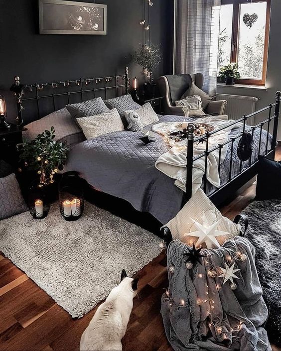 a moody bedroom with a black accent wall, a black metal bed with lights, potted plants and candles