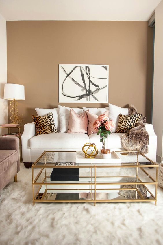 a neutral to muted living room with a white sofa, printed pillows, a printed artwork, a table lamp and a dusty pink sofa
