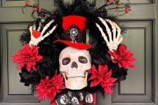 a red and black Halloween wreath of fabric blooms, feathers, branches, skeleton hands and a skull wearing a top hat