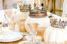 a refined white and gold Halloween tablescape with gold placemats, candleholders and crowns on pumpkins is amazing