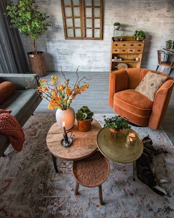 A rust colored chair, blanket, bright coffee tables and bold orange blooms add fall coloring to the living room
