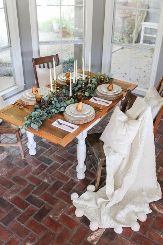 a simple Thanksgiving tablescape with tall candles, a greenery and pinecone runner, wood slices and pears on each place setting