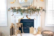 a white and gold Halloween fireplace with greenery, skulls, a skeleton, candles and bats