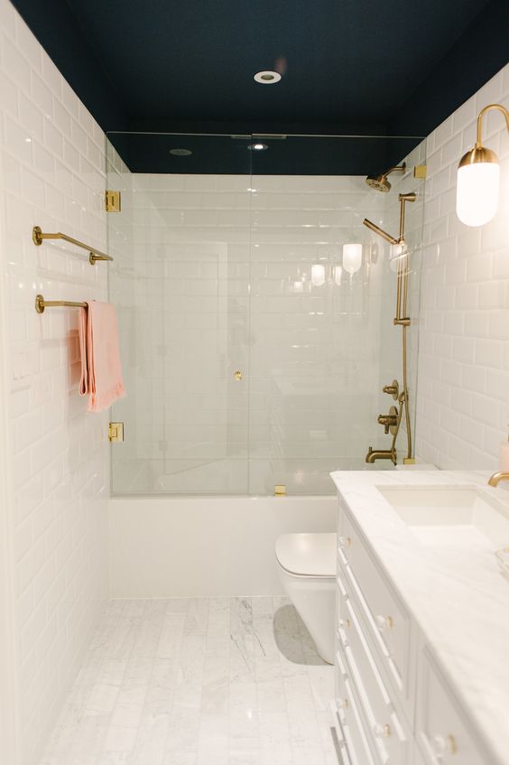 a white bathroom with a black ceiling, gold fixtures and gold sconces is a very chic and contrasting space