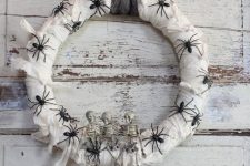 a white wrapped Halloween wreath covered with black spiders, skeletons and a black ribbon is a pretty and simple idea