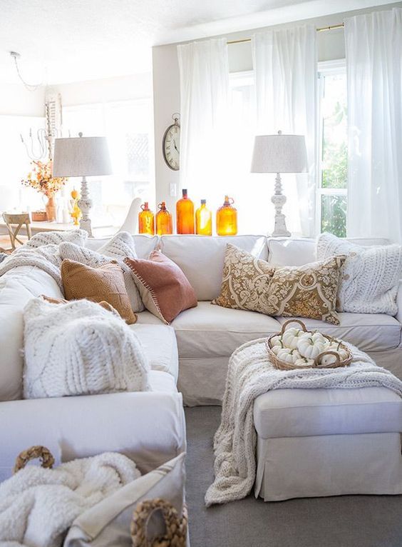Amber colored bottles and a basket with white pumpkins make this white living room more fall like