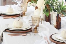 an elegant Thanksgiving table with wooden chargers, candles, amber glasses and apothecary bottles plus white pumpkins