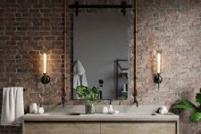 an industrial bathroom with brick walls, a wooden vanity with a stone sink, exposed pipes and wall sconces
