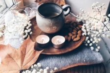 cozy and simple fall Nordic decor with a stack of blankets, baby’s breath and leaves, candles, nuts and coffee
