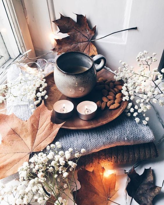 cozy and simple fall Nordic decor with a stack of blankets, baby's breath and leaves, candles, nuts and coffee