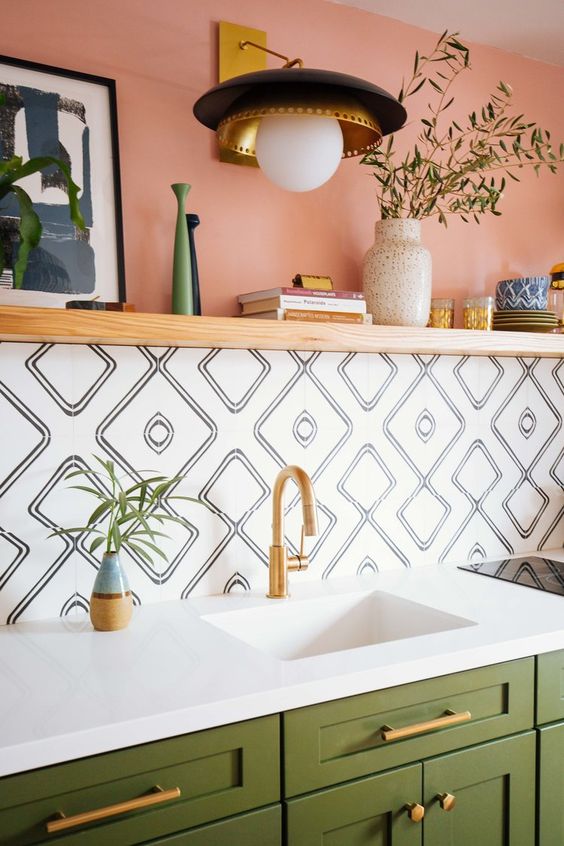 green cabinets, a color block wall with pink paint and catchy mosaic tiles, a white sink, gold fixtures and a gold and black sconce
