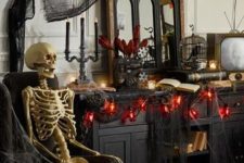 red and black Halloween decor with black cheesecloth, red lights, a cage with a crow and a skeleton