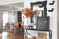 a Halloween console table with wheat and pumpkins, fall leaves in a glass vase, a chalkboard sign, black paper bats