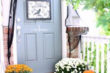 a Halloween front door with a black sign, skeleton hands and black spiderweb, a black mat and a blackbird plus pumpkins