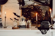 a Halloween mantel styled with black bats, a black wreath with lights, stacks of books, black branches and a black witch hat
