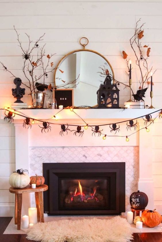 a Halloween mantel with a spider garland and string lights, a sign, a black house, blackbirds, branches and pumpkins around the fireplace