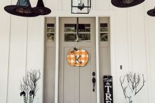 a Halloween porch decorated with witches’ hats and legs, branches, pumpkins, hay, blooms and a plaid sign on the door
