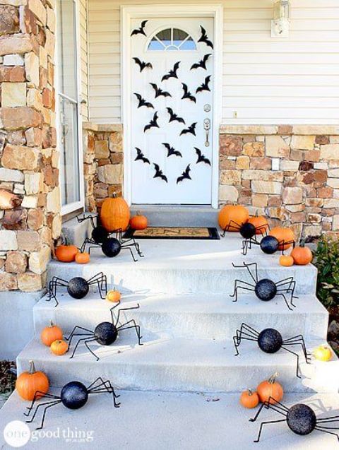 a Halloween porch with black bats on the door, orange pumpkins and fun black spiders is a fun and playful solution for the fall