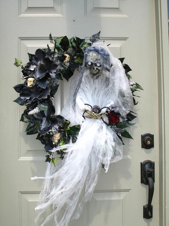 A black faux leaf and flower wreath with skulls, a ghost with a bloom is a very statement like and bold idea for Halloween