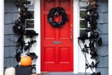 a black feather wreath, black ornaments, leaves and feathers framing the door, white and orange pumpkins for Halloween decor