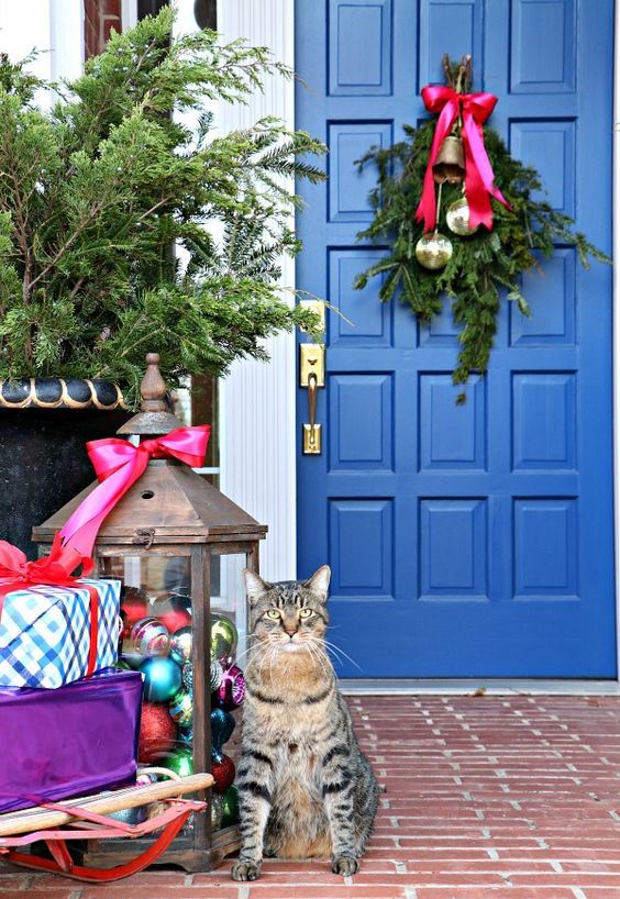 a bright Christmas porch with a large lantern filled with colorful ornaments, gift boxes and a posie with bells