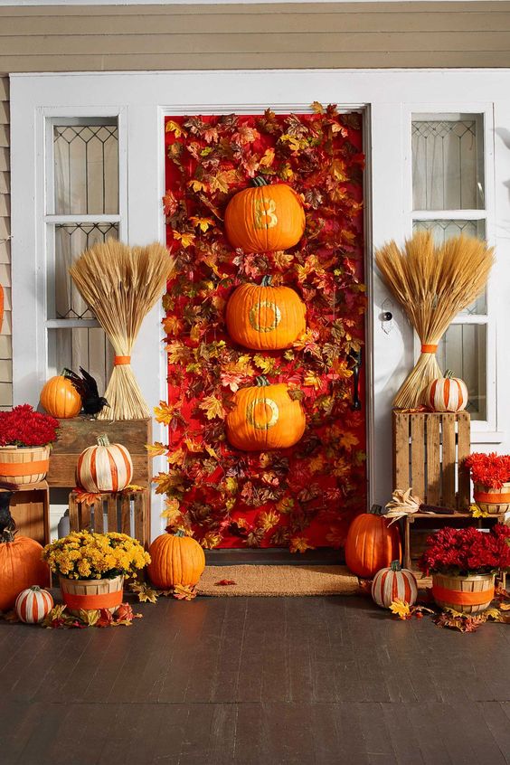 a bright Halloween porch with lots of pumpkins, bold blooms, wheat and a bold door covered with leaves and pumpkins with letters