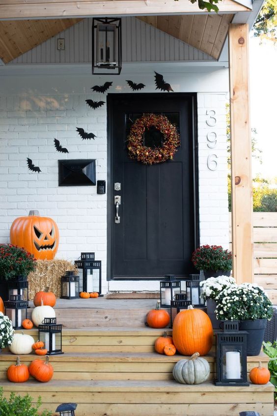 A bright rustic Halloween porch with bold and pastel pumpkins, blooms, hay, a giant jack o lantern, bats and a catchy fall colored wreath