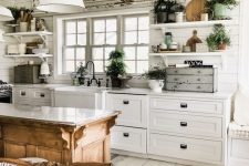 a charming white cottage kitchen with planked walls, shaker cabinets, corbel shelves and pendant lamps plus greenery