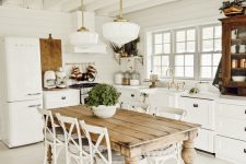 a charming white cottage kitchen with shaker style cabinets, a dining space with a stained table and vintage chairs plus pendant lamps