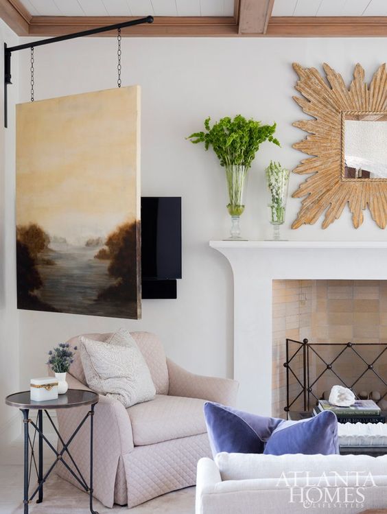 a coastal living room with a TV unit and an artwork hiding it, a fireplace, a mirror with an oranted frame and comfy seating furniture