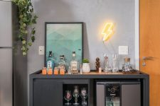 a contemporary home bar with a cabinet with glasses and wine bottles, a super modern wine cooler, a neon light, an ombre artwork and potted greenery