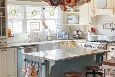 a creative cottage kitchen with light yellow cabinets, a blue kitchen island and neutral countertops, a hanger with copper pans and pots