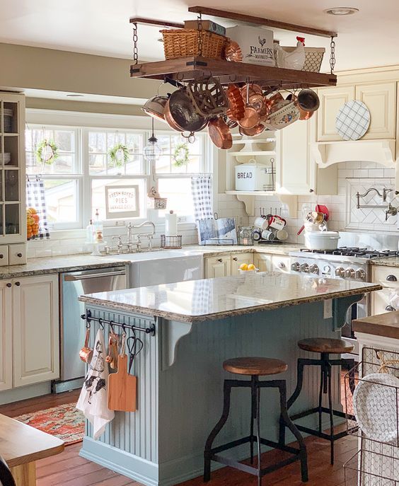 a creative cottage kitchen with light yellow cabinets, a blue kitchen island and neutral countertops, a hanger with copper pans and pots