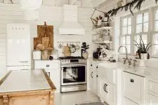 a cute cottage kitchen in white, with beadboard walls, shaker style cabinets, a stained kitchen island and wooden decor