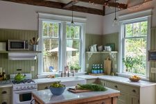 a cute green cottage kitchen with a beadboard backsplash, shaker cabinets, a stained kitchen island, wooden beams with lights