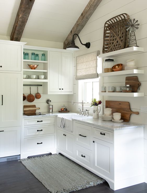 a cute little cottage kitchen with planked walls, open shelves, shaker cabinets, wooden beams and touches of stained wood decor